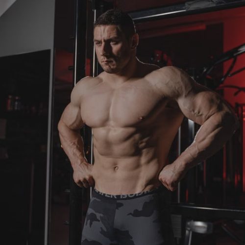Shirtless bodybuilder flexing muscles under dramatic gym lighting. Fitness and strength.